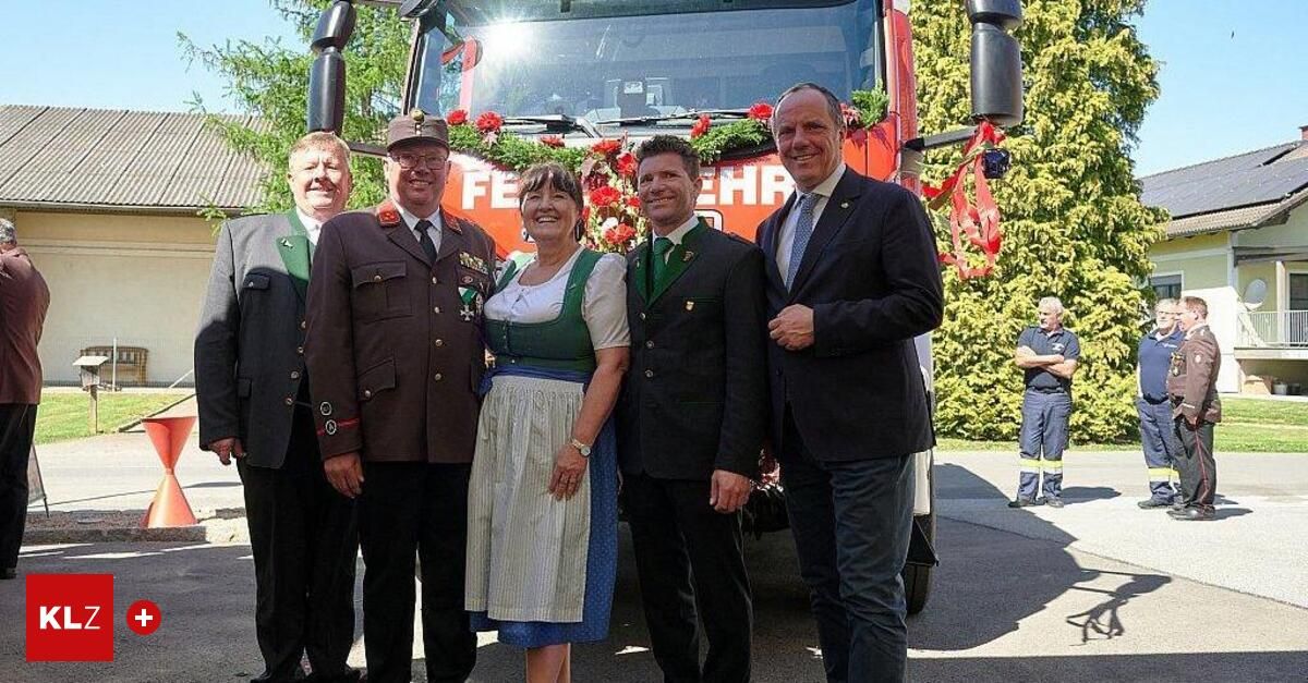 Fünf Personen, darunter drei Männer in Uniform, eine Frau in traditioneller Kleidung und ein Mann in Anzug, stehen vor einem Feuerwehrauto.
