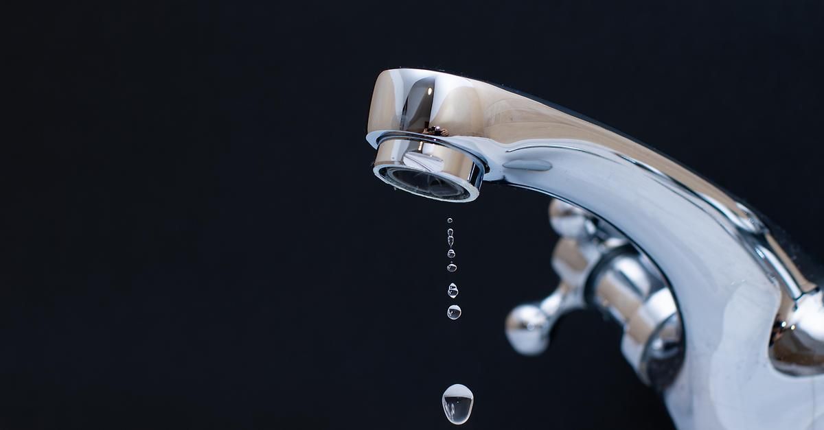 Ein Nahaufnahme eines Wasserhahns mit fallenden Wassertropfen vor schwarzem Hintergrund.