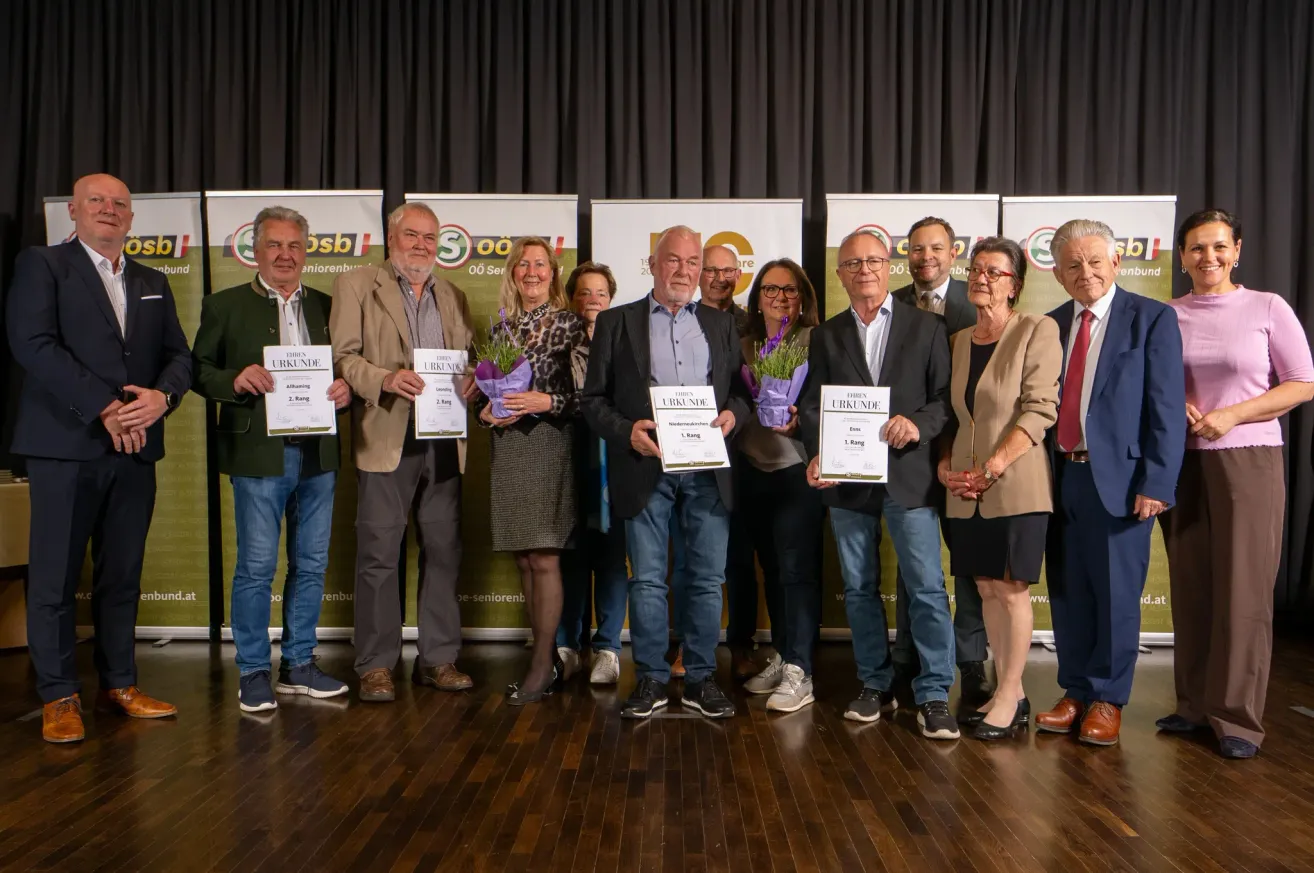 Eine Gruppe von Menschen, darunter Männer und Frauen, stehen zusammen und halten Urkunden. Sie scheinen eine Leistung zu feiern.