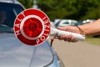 A person holding a red and white light that says 'HALT POLIZEI' in front of a parked car.