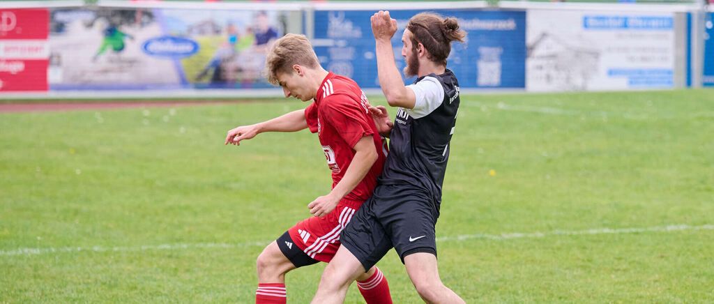 Zwei Fußballspieler, einer in Rot und einer in Schwarz, sind auf dem Feld in einen körperlichen Wettkampf verwickelt.