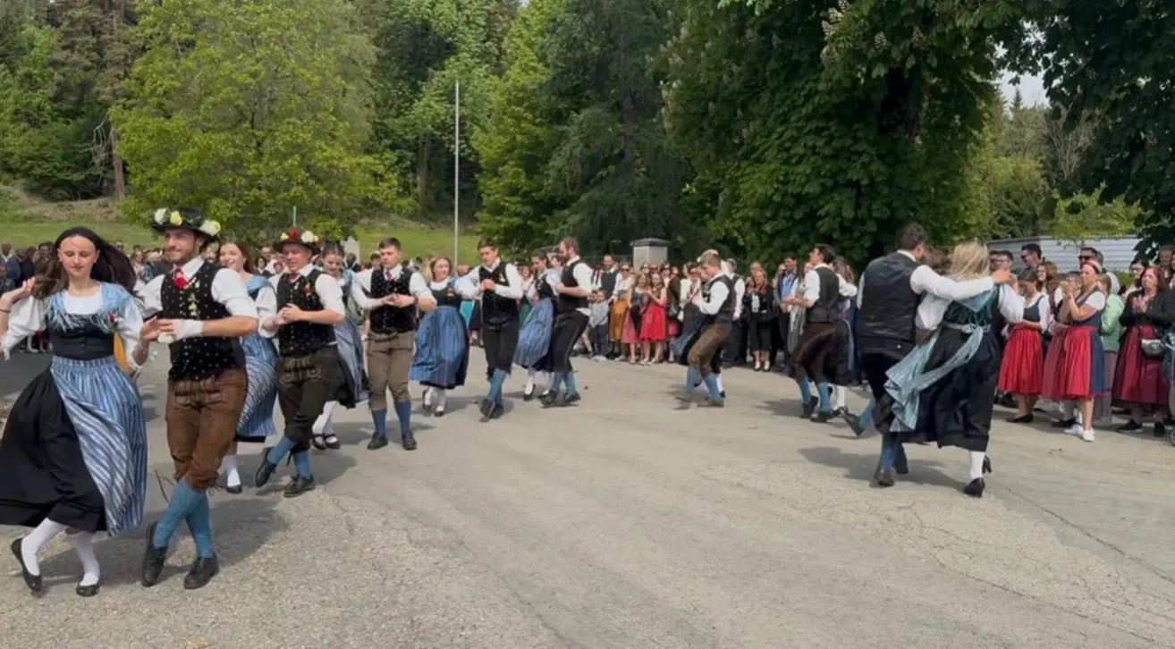 A group of people in traditional clothing is dancing on the road with onlookers watching on the side.