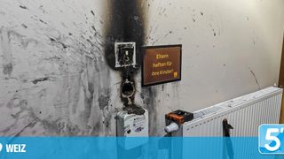 A burnt wall with a sign saying 'Parents have to take care for their children', damaged electrical installations and a damaged radiator.