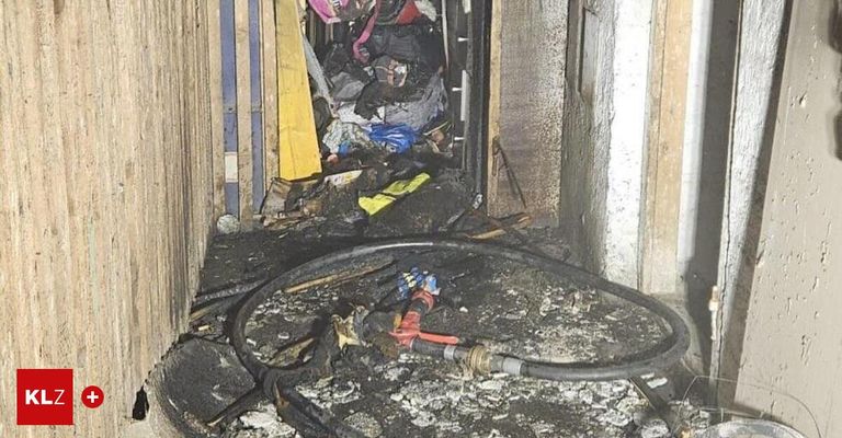 The interior of a building shows debris and a fire hose on the ground. The walls are charred, and scattered items suggest a fire's aftermath.