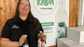 A woman stands in front of a banner advertising Kabia wine. She holds two bottles, one labeled Terold, and smiles at the camera.