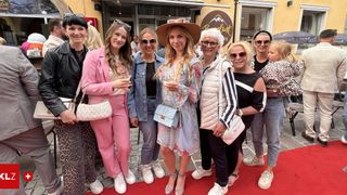 A group of women and a child stand on a red carpet in front of a building. They are smiling and appear to be posing for a photo.