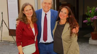 Three people are smiling and posing for a photograph. A man is standing between two women.