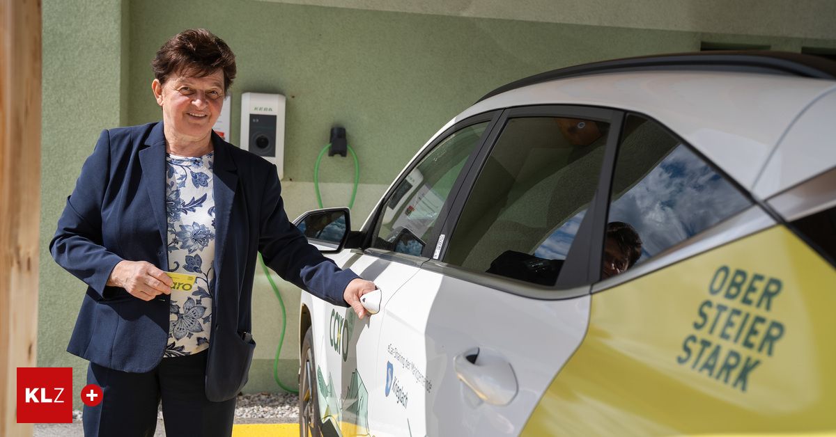 Eine Frau hält eine Karte neben einem gelben und weißen Auto mit angeschlossenem Ladekabel.