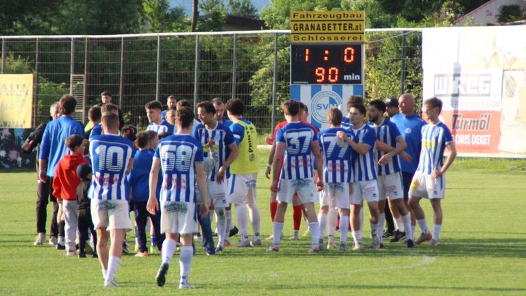 Soccer players in blue and white uniforms gather on a field. The scoreboard shows a score of 1:0. The time is 90 minutes.