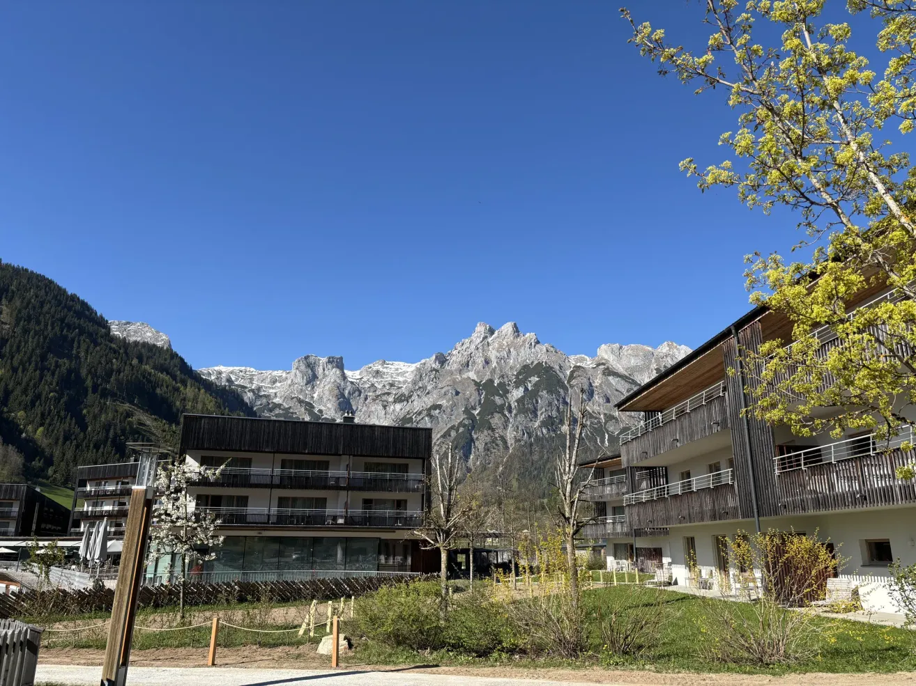 Moderner Gebäudekomplex mit Balkonen am Fuße verschneiter Berge unter einem klaren blauen Himmel.