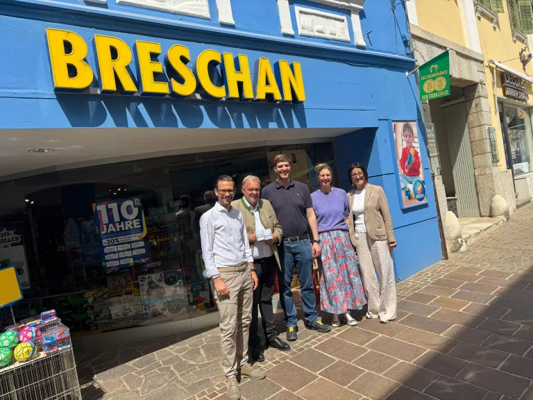 Five people are standing outside a store named Breschan. A sign shows 110 years and a 20% discount.