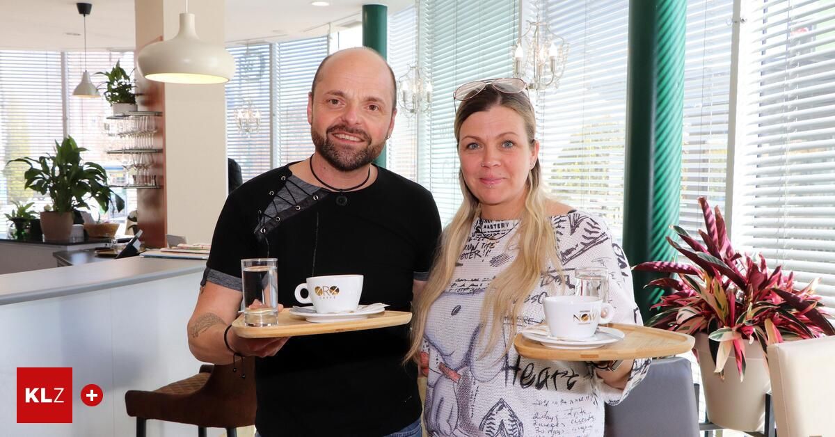 A man and a woman are smiling and posing with trays of coffee cups and glasses of water in a restaurant.
