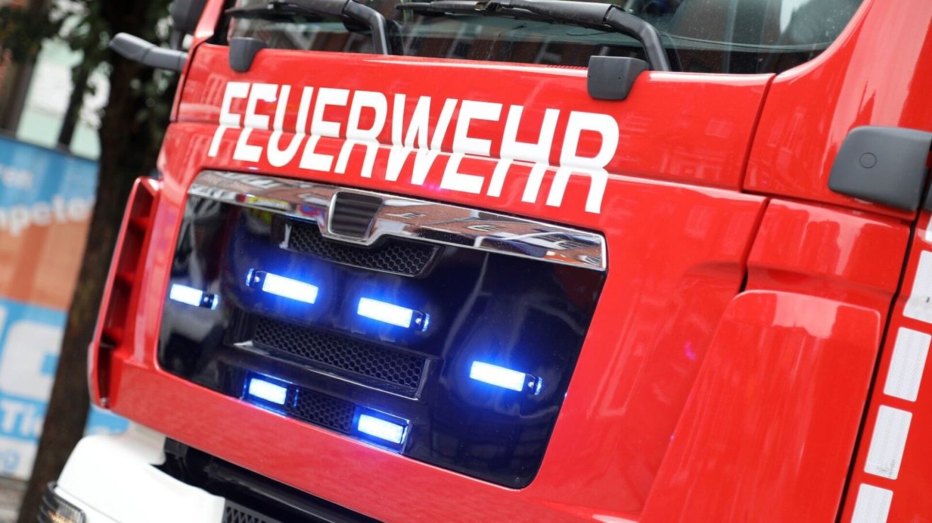 Ein rotes Notfallfahrzeug mit der Aufschrift 'FEUERWEHR' hat blaue Lichter auf der vorderen Stoßstange. Die Lichter sind an und blinken.