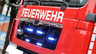 A red emergency vehicle with the word 'FEUERWEHR' on it has blue lights on the front bumper. The lights are on and flashing.