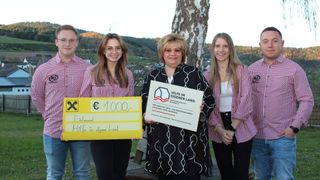Eine Gruppe von vier Menschen steht im Freien und lächelt. Eine Frau hält einen gelben Scheck über 1000 Euro. Eine andere Frau hält ein Schild mit der Aufschrift Hilfe im eigenen Land.