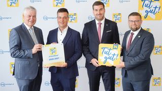 Four men in suits holding signs that say Tut gut! One man holds a gold plaque for 2026-2027. They stand in front of a white wall with logos.