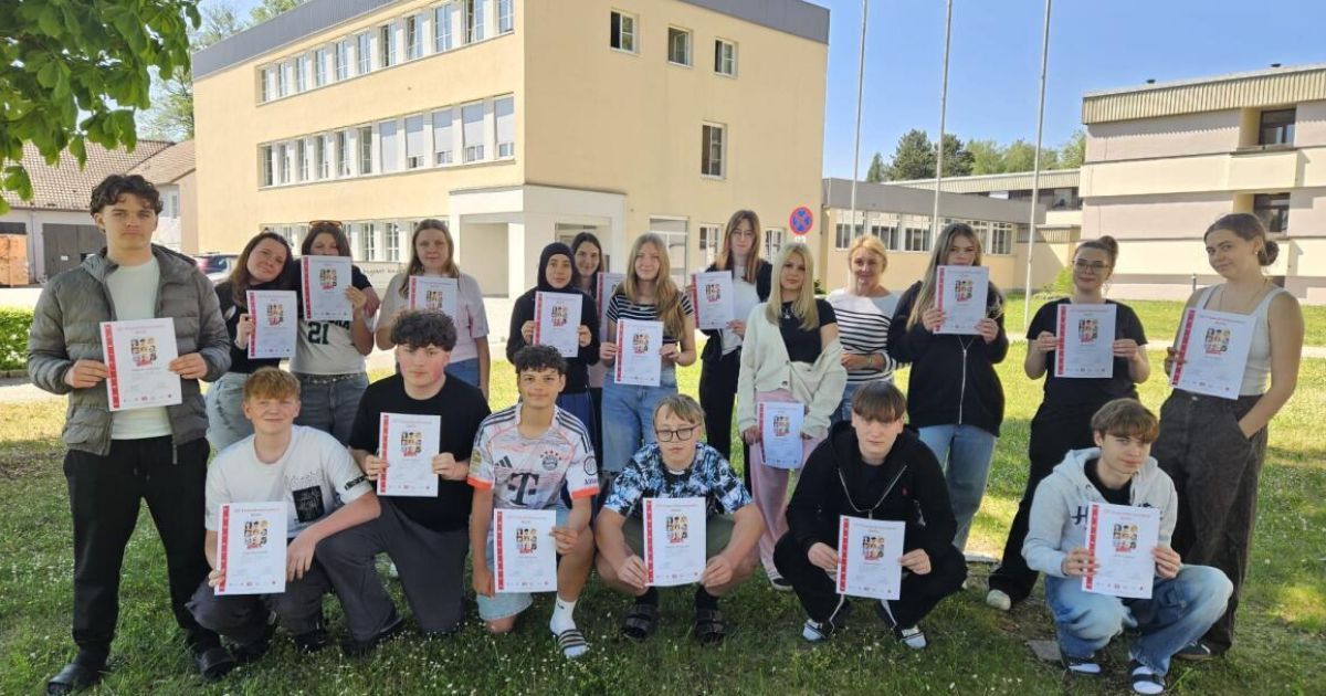 Eine Gruppe junger Menschen posiert für ein Foto, während sie Urkunden vor einem Gebäude halten.