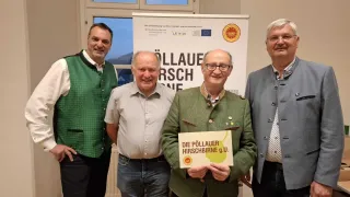 Four men stand in front of a banner with the words 'Ollaue Hirschbirne'. The man in the middle holds a sign that reads 'Die Pollauer Hirschbirne g.U.' They all appear to be smiling.