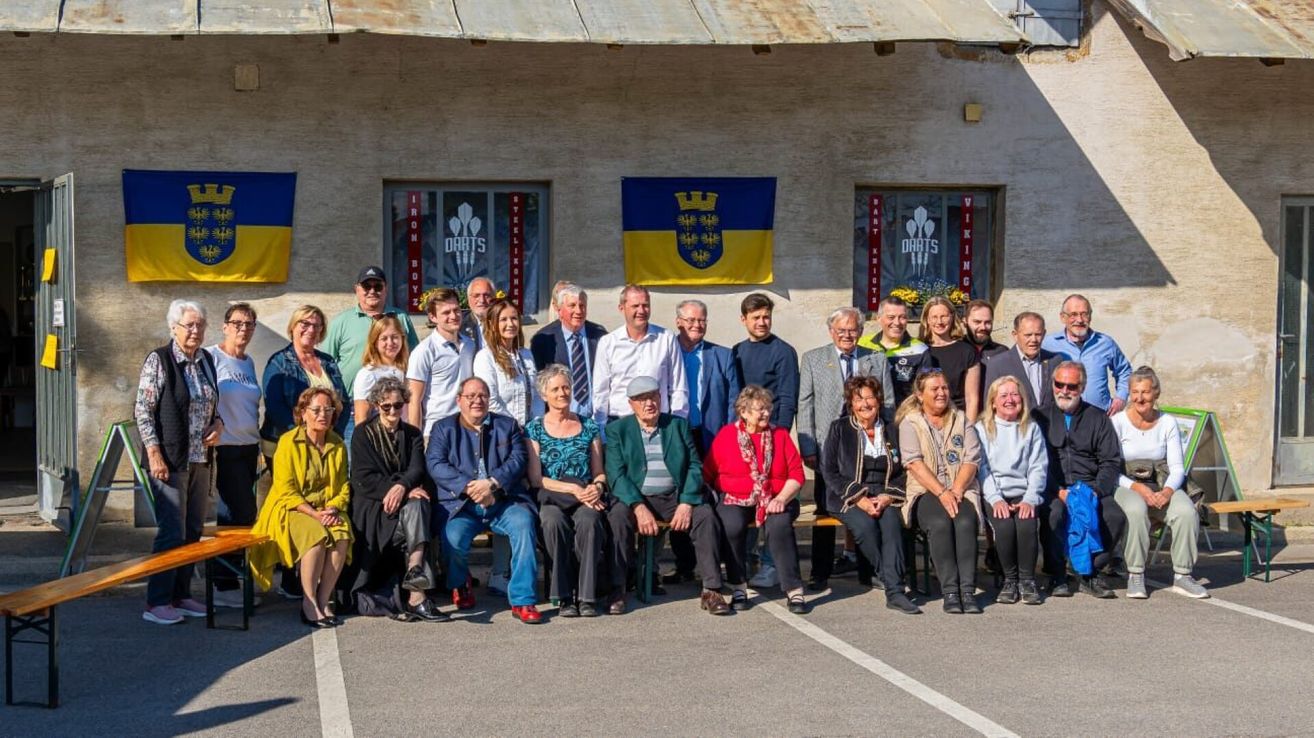 Eine Gruppe von Menschen ist vor einem Gebäude mit einer Ukraine-Flagge versammelt, einige sitzen und einige stehen, lächeln für ein Foto.