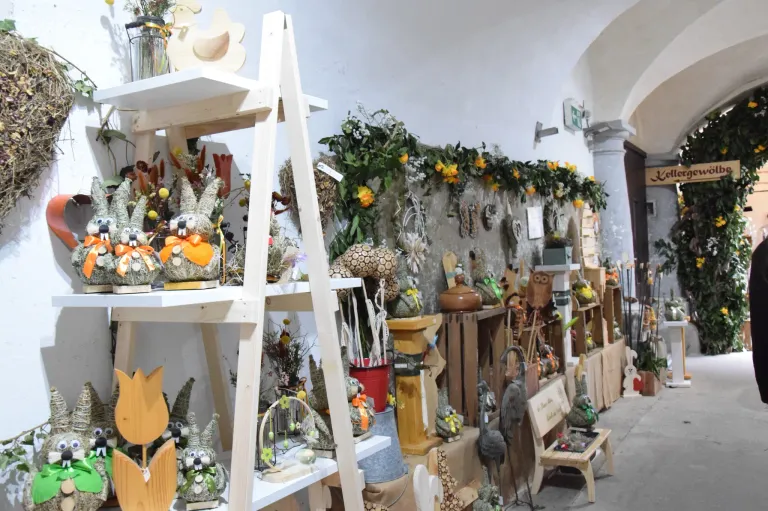 Ein Raum gefüllt mit verschiedenen dekorativen Gegenständen. Ein Holzleiter hält Ornamente, und die Wand ist mit grünen Girlanden geschmückt. Verschiedene Gegenstände sind auf Regalen und Tischen ausgestellt.