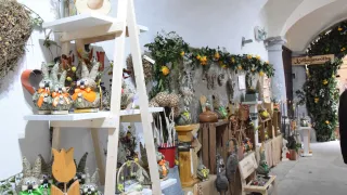 Ein Raum gefüllt mit verschiedenen dekorativen Gegenständen. Ein Holzleiter hält Ornamente, und die Wand ist mit grünen Girlanden geschmückt. Verschiedene Gegenstände sind auf Regalen und Tischen ausgestellt.