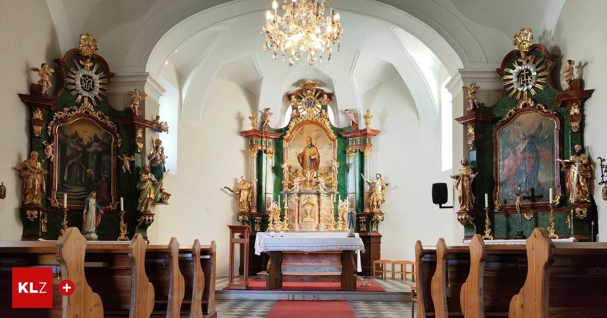 A church interior with a large ornate altar, statues, and a chandelier. Pews are arranged, and a red carpet leads to the altar.