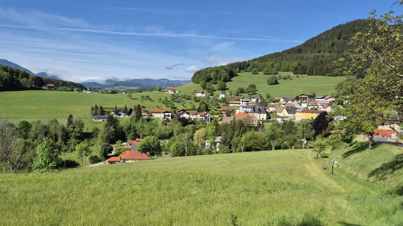 A picturesque village nestled in a valley surrounded by lush green hills and mountains, under a clear blue sky.