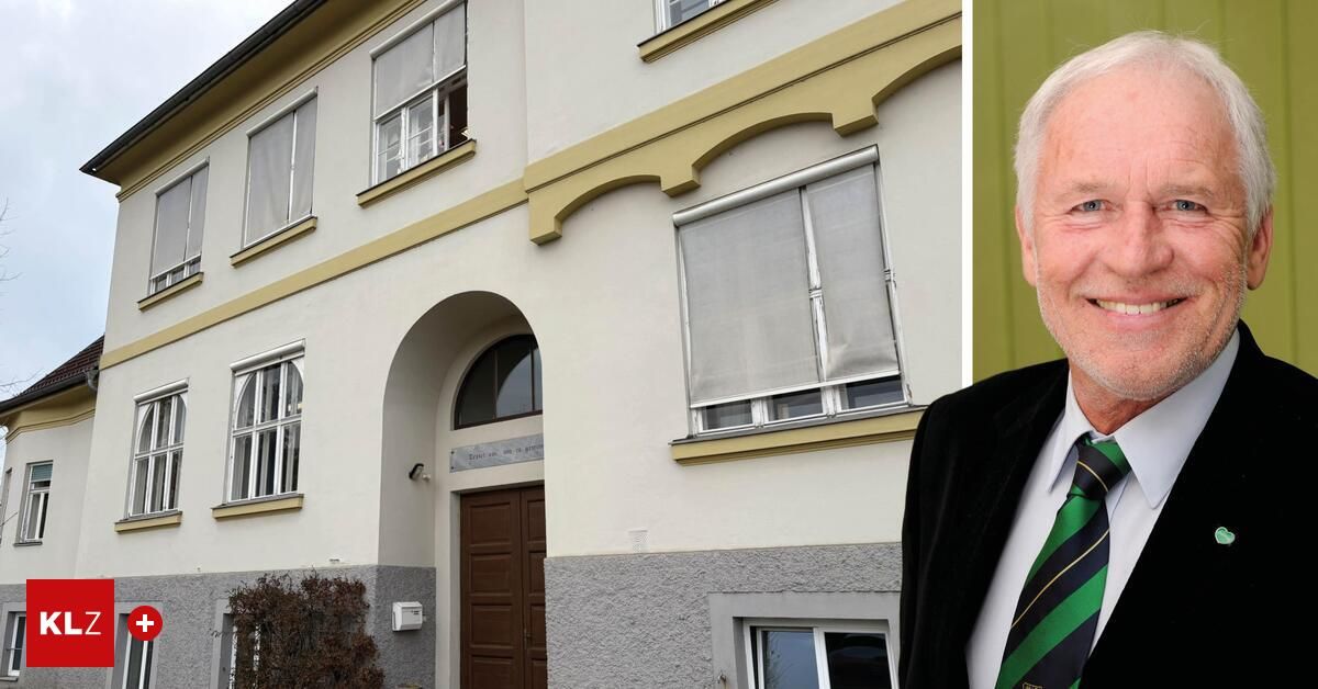 Ein Mann in Anzug steht neben einem Gebäude mit Fenstern, einer geschlossenen Tür und einem Bogen. Das Gebäude ist weiß gestrichen und mit gelbem Rand verziert.