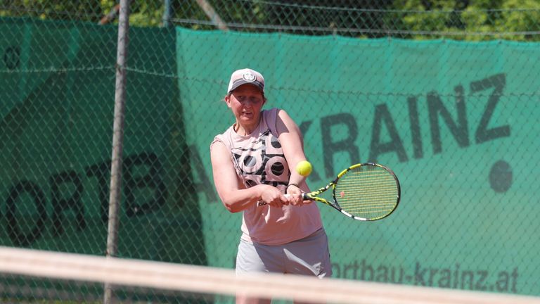 A woman is playing tennis on a court. She wears a hat and a shirt with a black and white design. She swings her tennis racket to hit the ball.