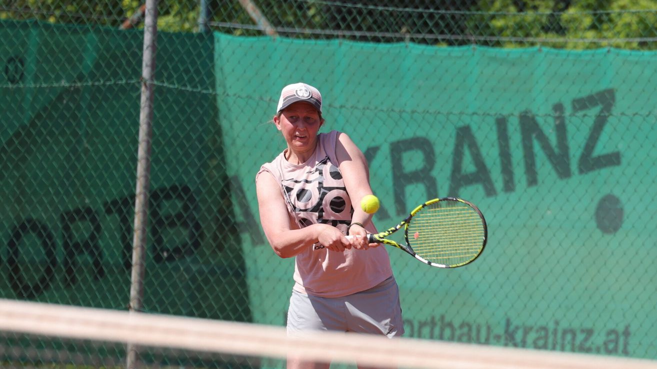 A woman is playing tennis on a court. She wears a hat and a shirt with a black and white design. She swings her tennis racket to hit the ball.