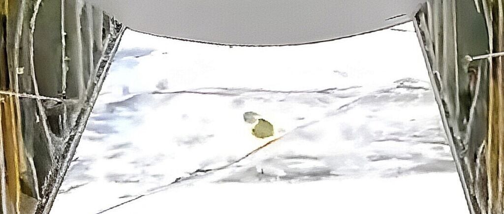 Eine verschneite Landschaft mit einem kleinen, abgerundeten Objekt, das teilweise im Schnee vergraben ist. Der Himmel ist grau, und es sind keine Bäume oder Strukturen sichtbar.