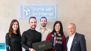 Fünf Personen stehen vor einem Schild, das 'Vorne sein im Internet' sagt. Der Mann auf der linken Seite hält eine Box. Die Frau auf der rechten Seite trägt eine Brille und einen Schal. Der Mann in der Mitte trägt ein weißes Hemd.