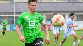 Ein Fußballspieler in einem grünen Trikot mit der Nummer B läuft auf dem Feld, ein Ball in der Luft.