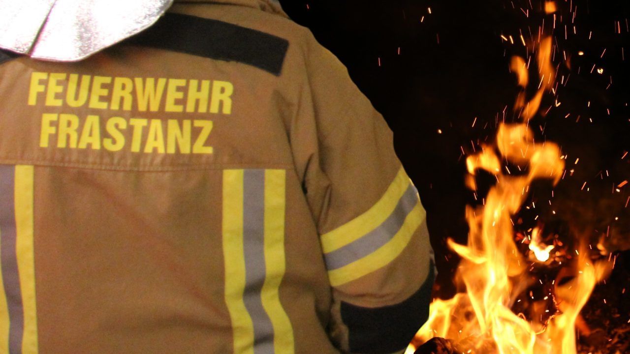 A firefighter in a uniform with the word Wehr on the back stands near a fire at night.