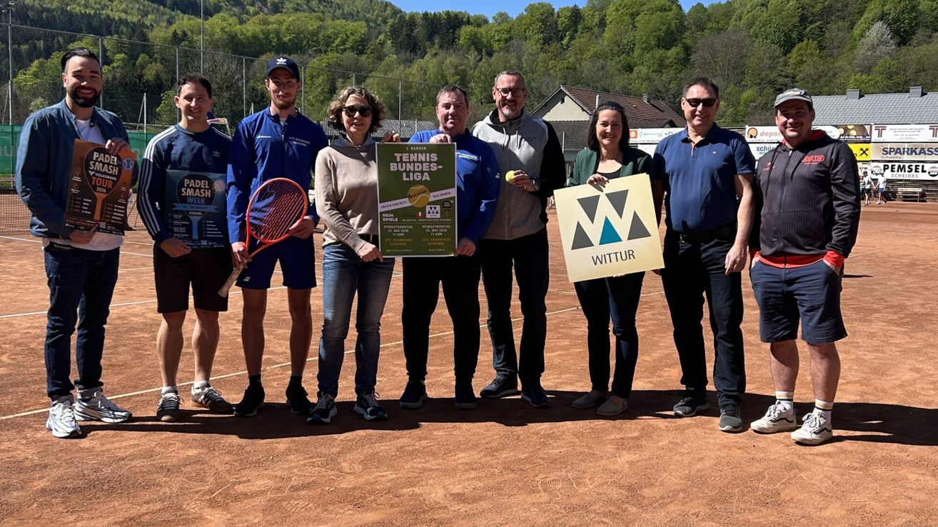 Eine Gruppe von Menschen steht auf einem Tennisplatz und hält ein Schild mit der Aufschrift Tennis Bundesliga. Sie lächeln und scheinen für ein Foto zu posieren.