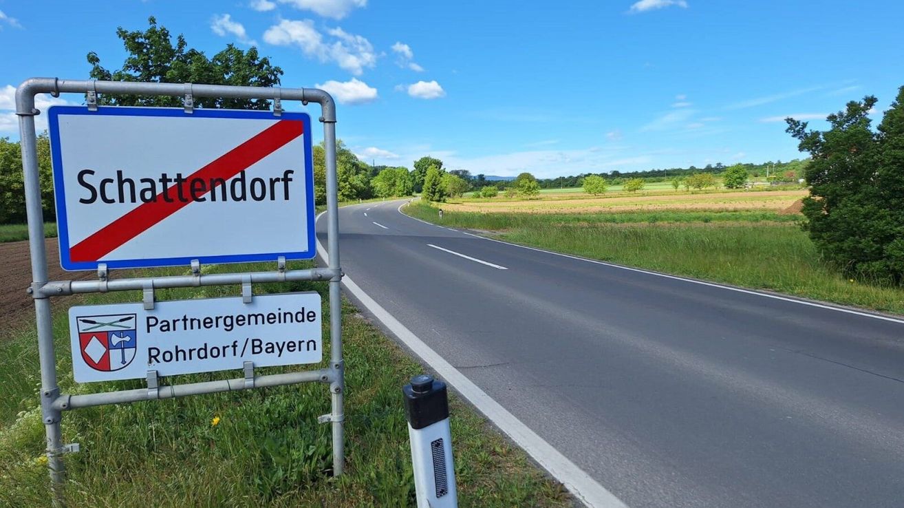 Ein Straßenschild für Endorrf, ein Dorf in Bayern, steht am Straßenrand, mit einem weiten grünen Feld, das sich unter einem klaren blauen Himmel erstreckt.