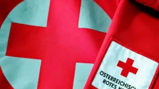 Ein Nahaufnahme eines roten Kreuzes auf rotem Hintergrund. Das Kreuz befindet sich in einem Kreis mit weißem Rand.