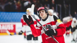 Ein Eishockeyspieler in rot-weißem Trikot feiert auf dem Eis und hält einen Schläger in der Hand, während andere Spieler im Hintergrund stehen.