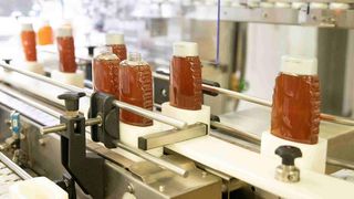 Mehrere Flaschen mit roter Flüssigkeit befinden sich auf einer automatischen Montagelinie in einer Fabrikumgebung.