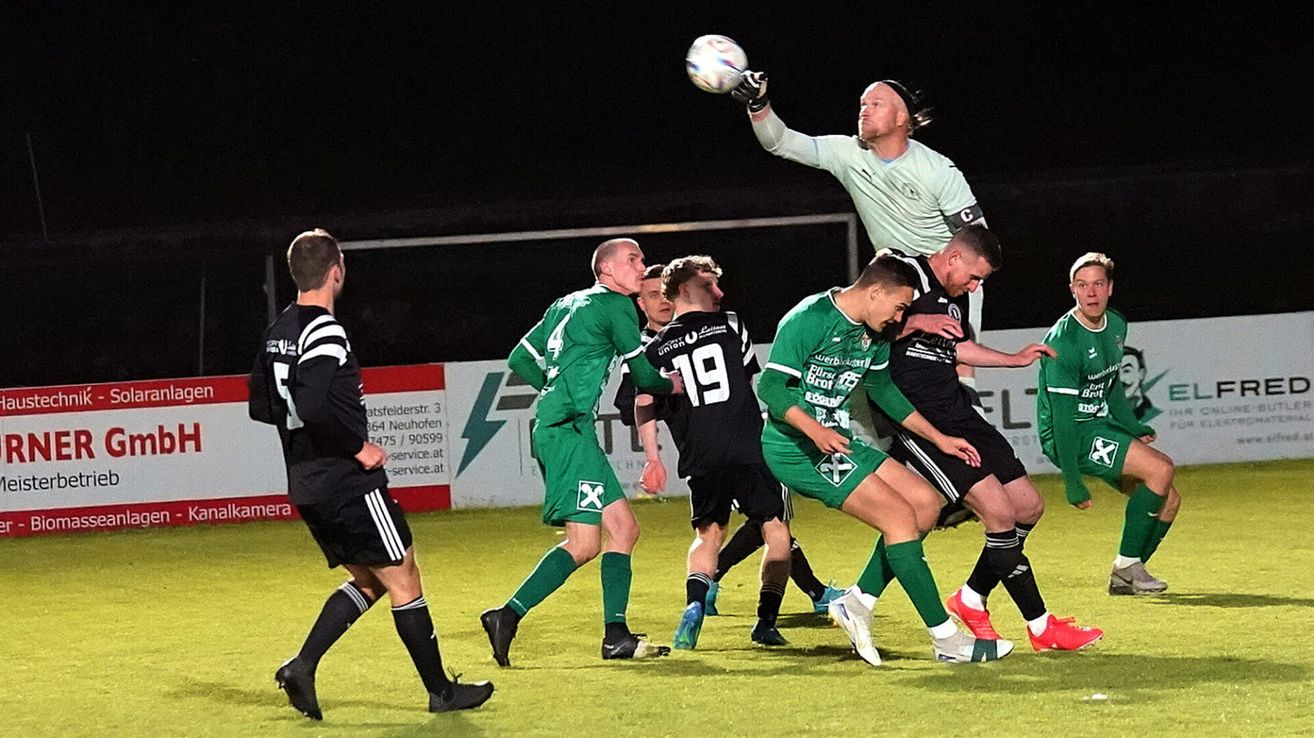 Fußballspieler in grünen und schwarzen Trikots spielen nachts auf einem Feld. Ein Spieler in Grün versucht, den Ball zu fangen.
