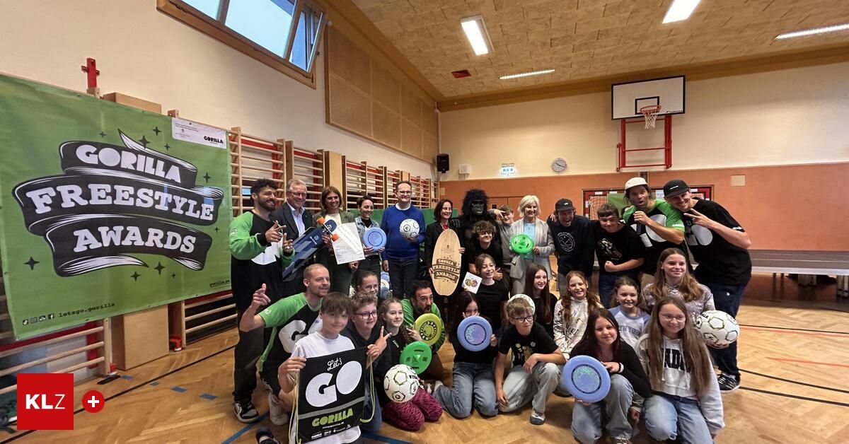 Eine Gruppe von Menschen in einer Turnhalle mit einem Basketballkorb. Sie halten ein Frisbee, einen Ball und ein Zertifikat. Einige von ihnen sitzen auf dem Boden, während andere stehen. Der Raum hat einen Holzboden und eine weiße Wand mit einer Uhr und einem Plakat.