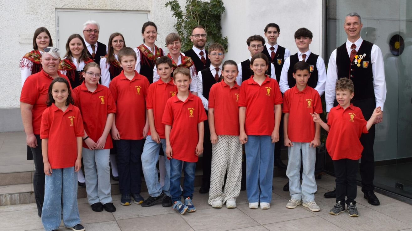 A group of children and adults in red polo shirts are posing for a photo outside. They stand in two rows, with a few adults behind them.