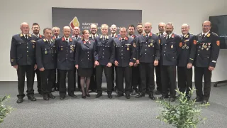 Eine Gruppe uniformierter Personen steht vor einem großen Schild. Sie lächeln und posieren für ein Foto.