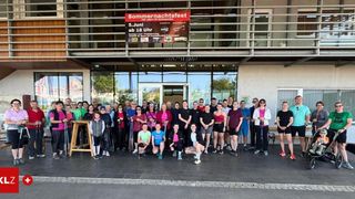 Eine große Gruppe von Menschen steht vor einem Gebäude und hält Stöcke, wahrscheinlich für eine Sportveranstaltung. Ein Banner oben zeigt 'Sommernachtsfest'.