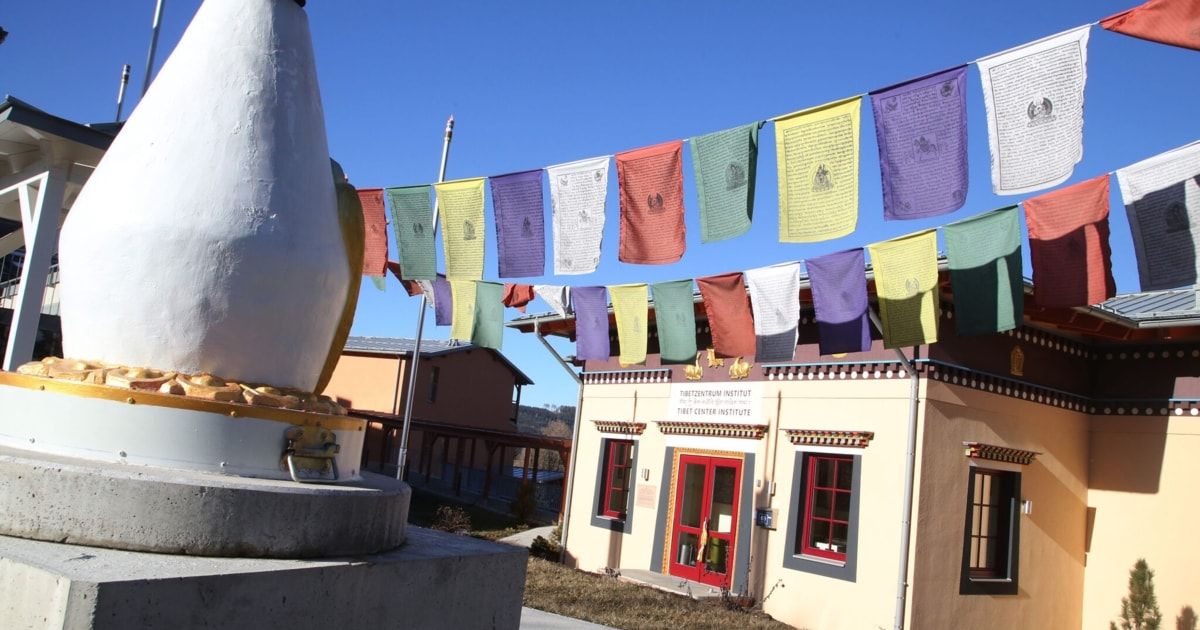 Ein tibetisches Zentrumsinstitut mit roter Tür, bunten Gebetsfahnen und einer großen weißen Statue davor.