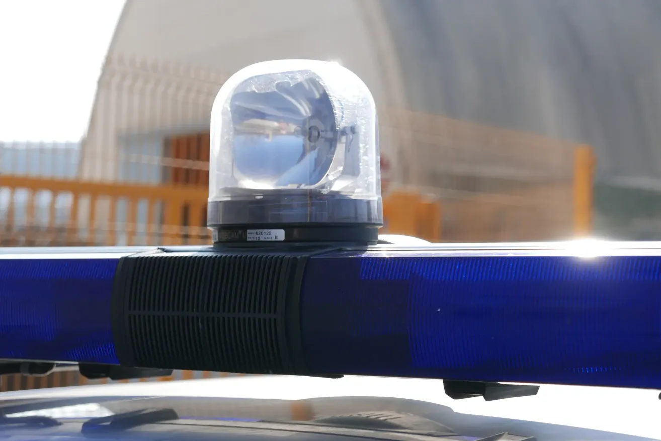 Eine Nahaufnahme eines blauen Polizeiwagens mit blinkender Lampe an einem sonnigen Tag. Die Lampe besteht aus klarem Kunststoff mit einer reflektierenden Oberfläche.