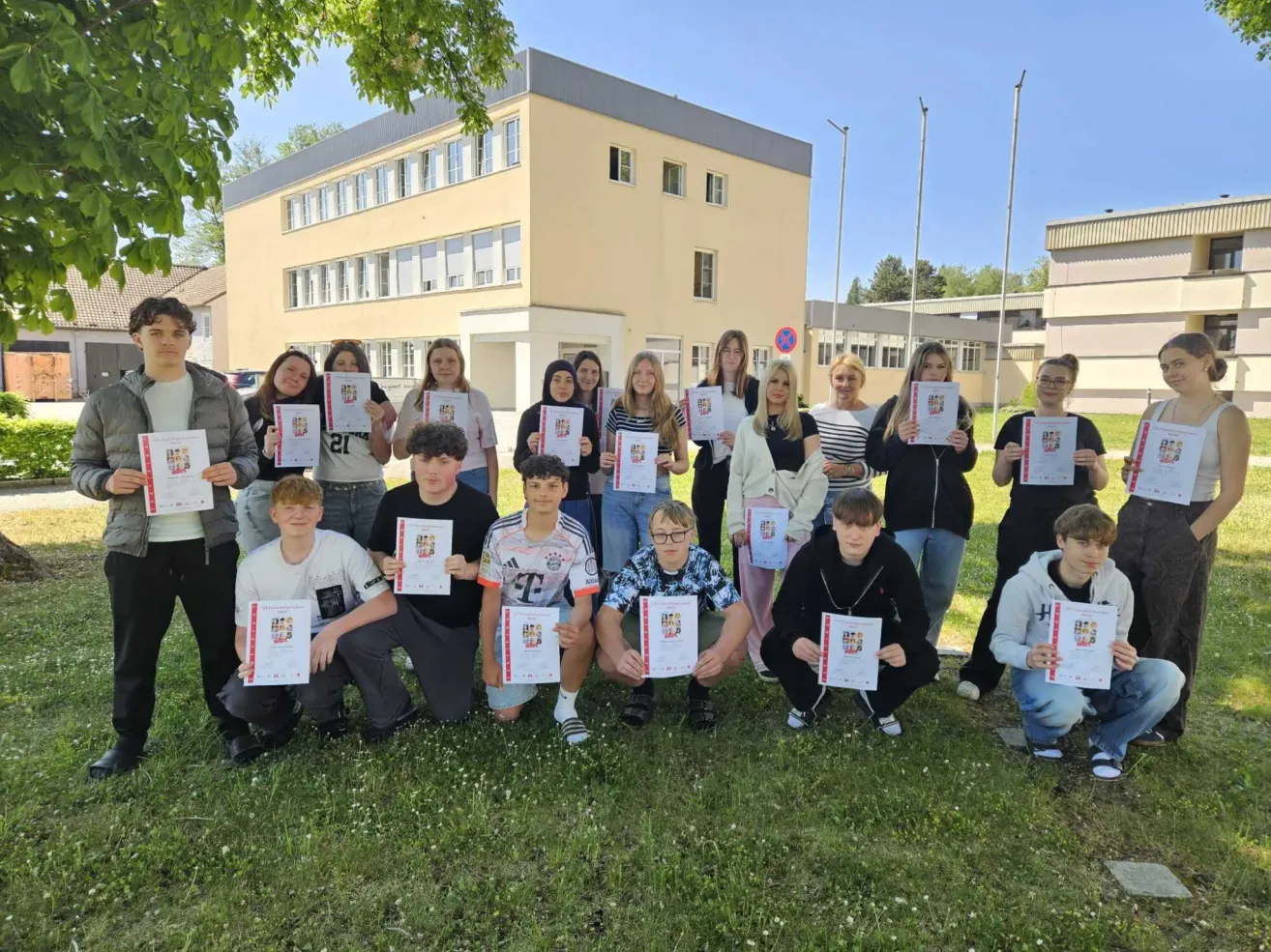 Eine Gruppe von Schülern posiert für ein Foto vor einem Schulgebäude und hält Urkunden in den Händen.