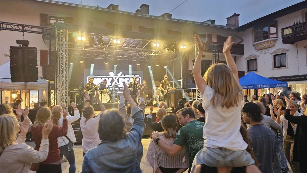 A band is performing on a stage with spotlights. A crowd of people, including a girl and a man, are cheering.