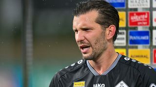 A male soccer player with a serious expression is shouting. He wears a black jersey with white stripes and a yellow patch.