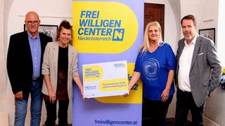 Zwei Frauen stehen hinter einem Banner mit der Aufschrift 'Freiwilligen Center Niederosterreich'. Eine hält ein Schild mit 'Fachngeuten 2026', die andere lächelt. Sie tragen beide blaue Shirts.